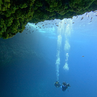 Two scuba divers ascending with bubbles under rocky overhang, Cape Verde